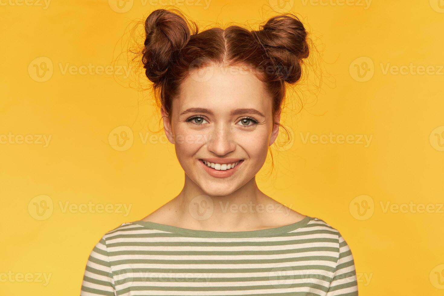 joven dama, bonito, encantador jengibre mujer con dos bollos y sano piel. siente felicidad. vistiendo a rayas suéter y acecho a el cámara aislado, de cerca terminado amarillo antecedentes foto