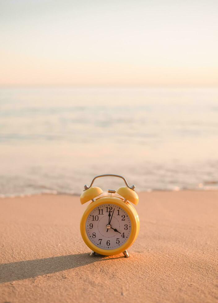 Yellow alarm clock on the beach in the sunset time. The concept about Time to summer, Travel, Vacation and Relaxation photo