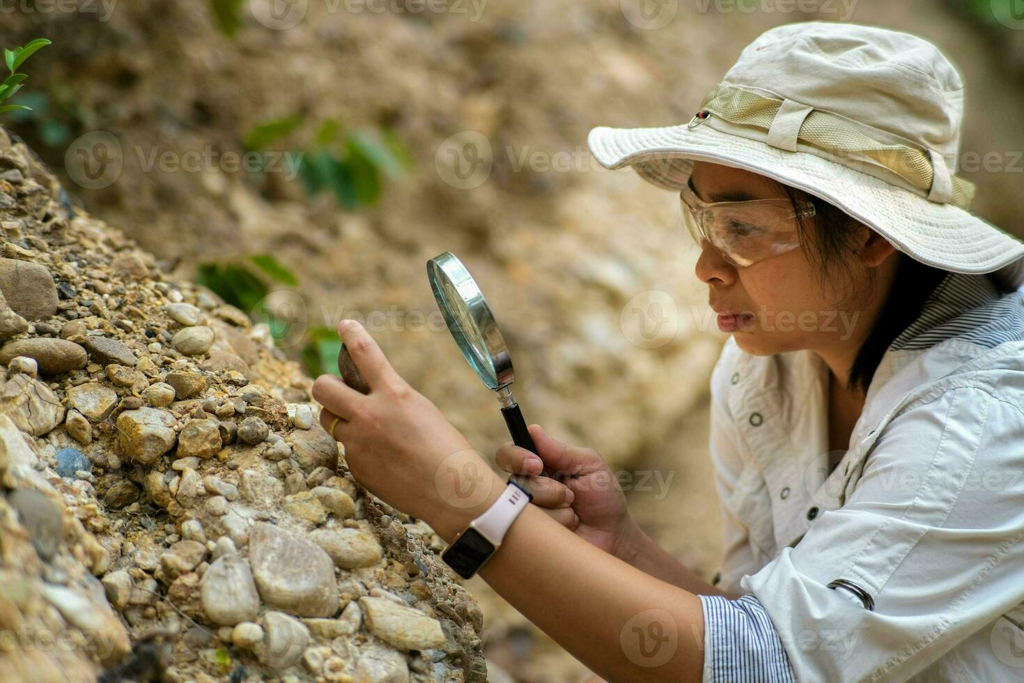 Female geologist using magnifying glass to examine and analyze rock, soil, sand in nature. Archaeologists explore the field. Environmental and ecology research. photo