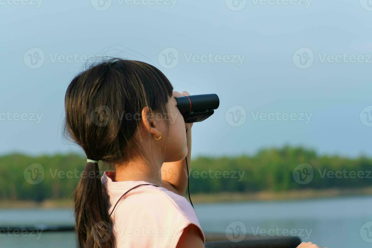 Little girl looking through binoculars at birds on the reservoir. Explore and adventure concept. Birdwatching photo