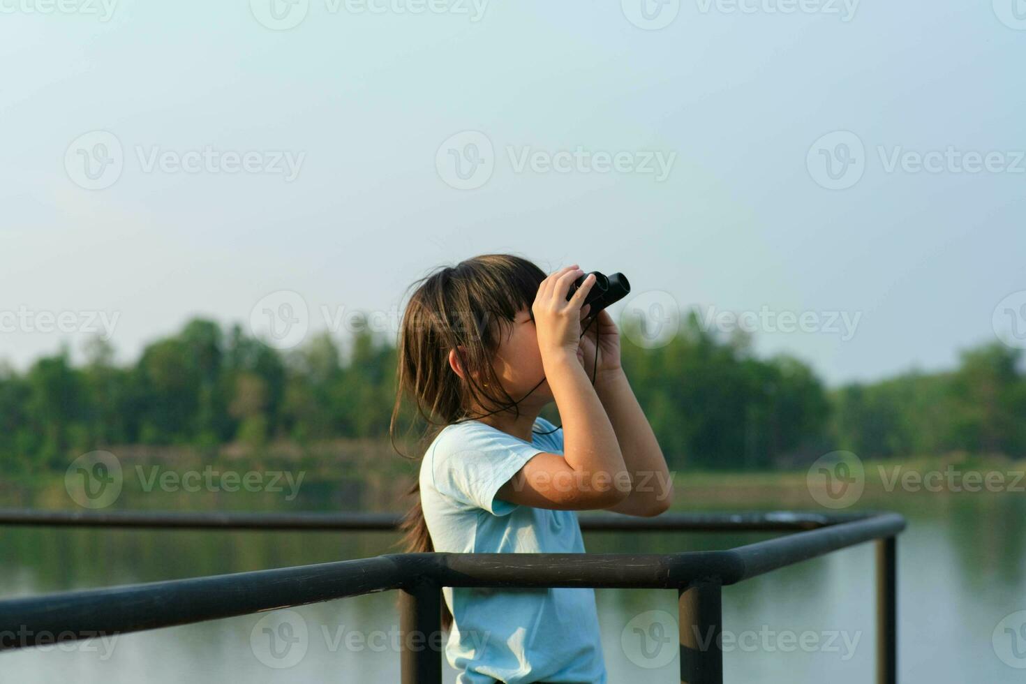 Little girl looking through binoculars at birds on the reservoir. Explore and adventure concept. Birdwatching photo