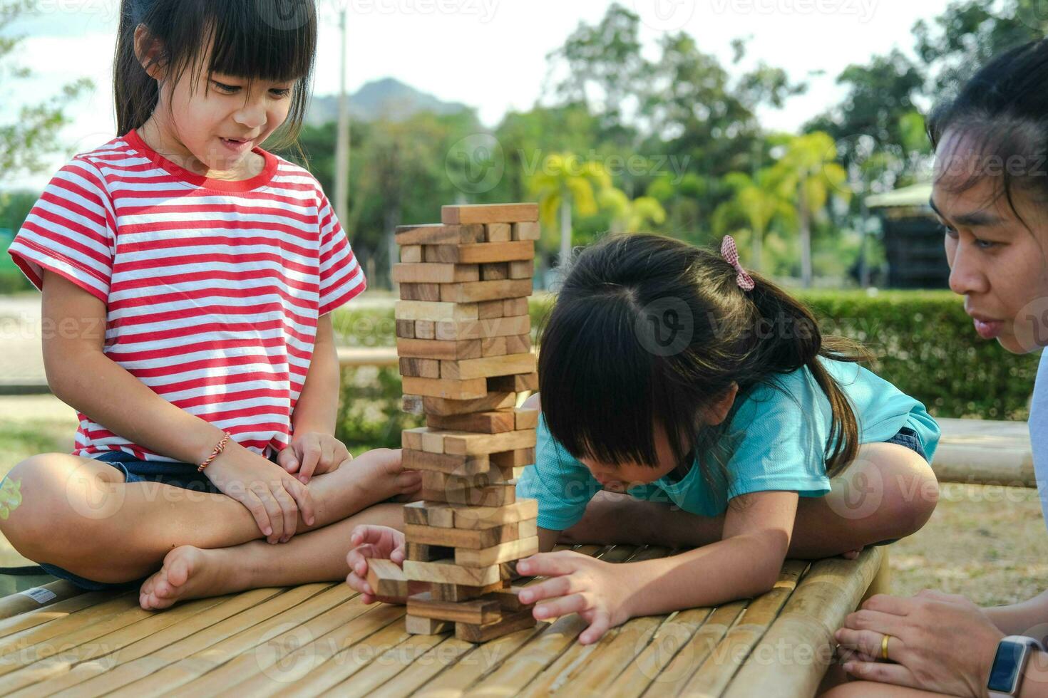 niños emocionados y mamá jugando al juego de bloques de madera de la torre jenga juntos en el parque. familia feliz con niños disfrutando juntos de las actividades de fin de semana. foto