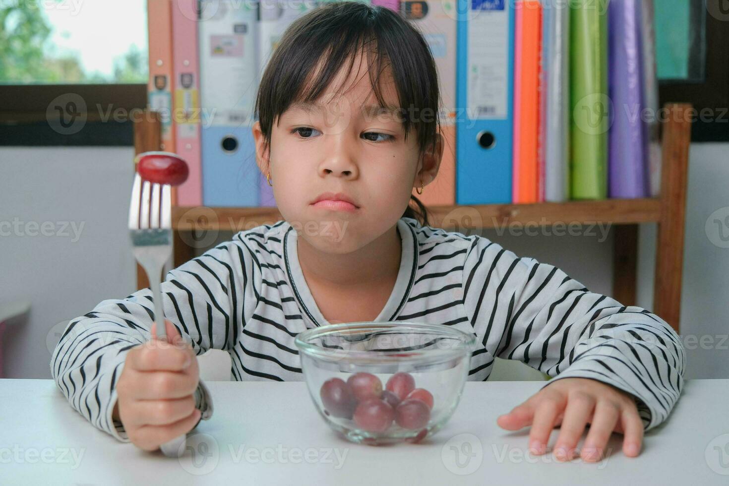 Children don't like to eat fruits. Cute young Asian girl refusing to eat healthy fruits. Nutrition and healthy eating habits for children. photo