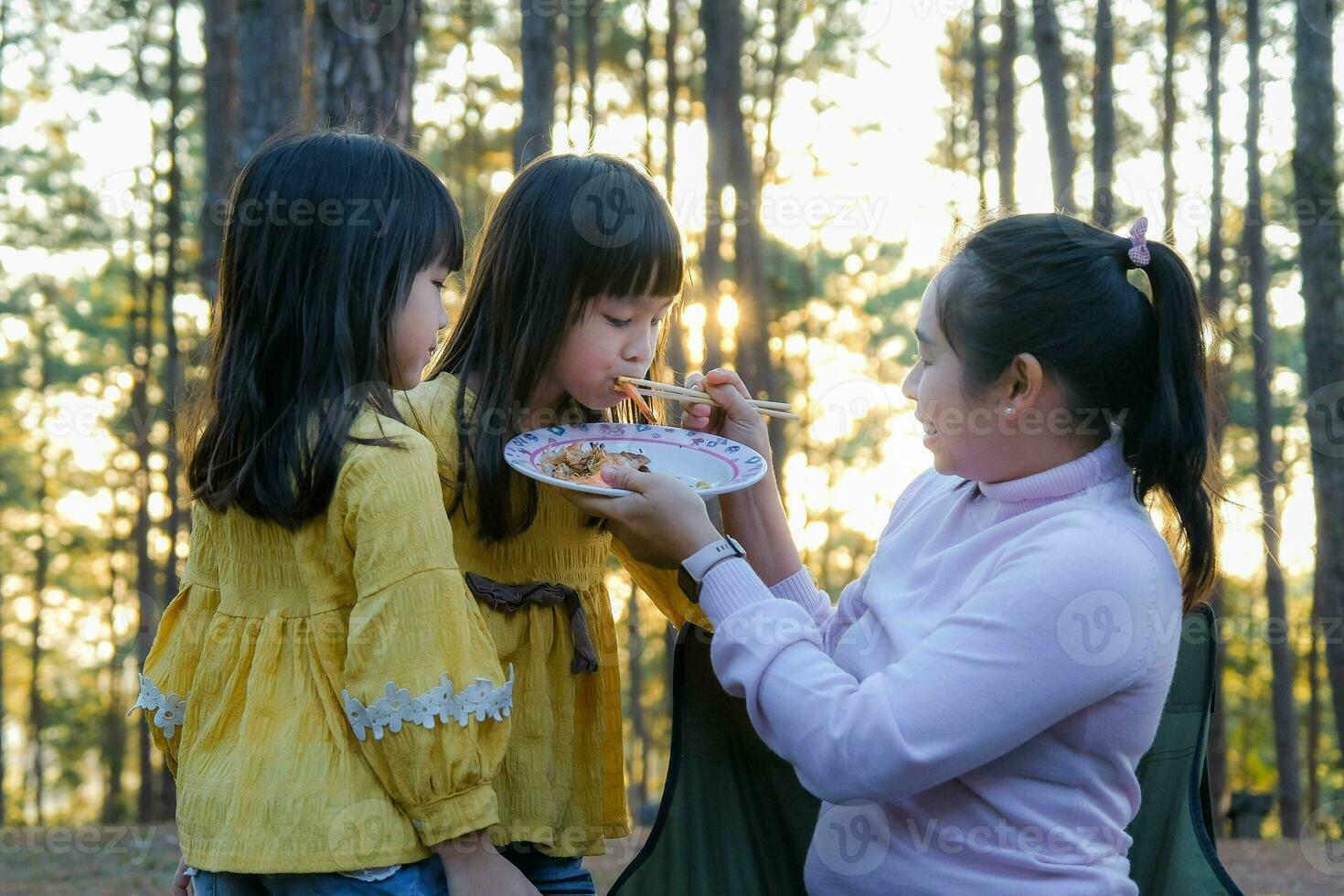 Happy mother and children picnic sit by stove near tent and grill a barbecue in pine forest, eating and have conversation. Happy family on vacation in nature. photo