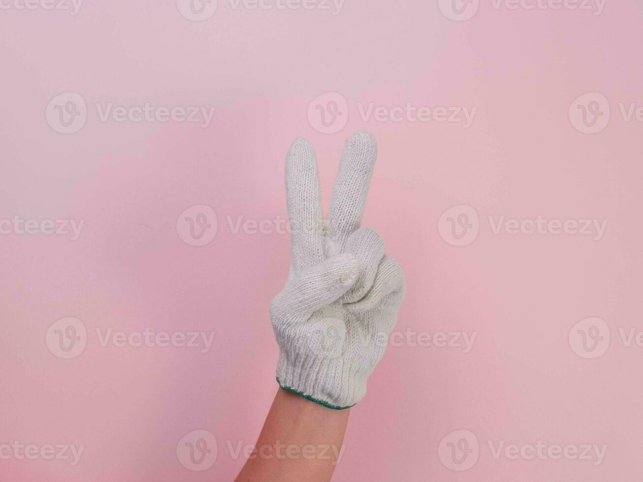 Hands in white knitted gloves isolated on pink background. Female hand holding up two fingers peace symbo with cotton glove. photo