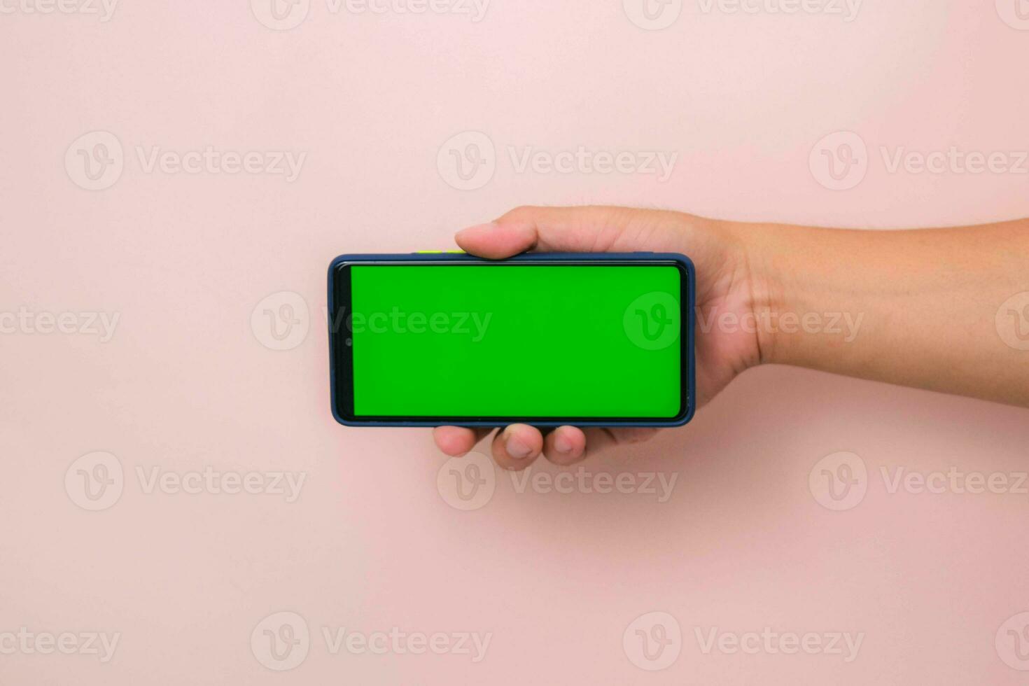 Human hand holding mobile smartphone with green screen in horizontal position isolated on pink background. photo