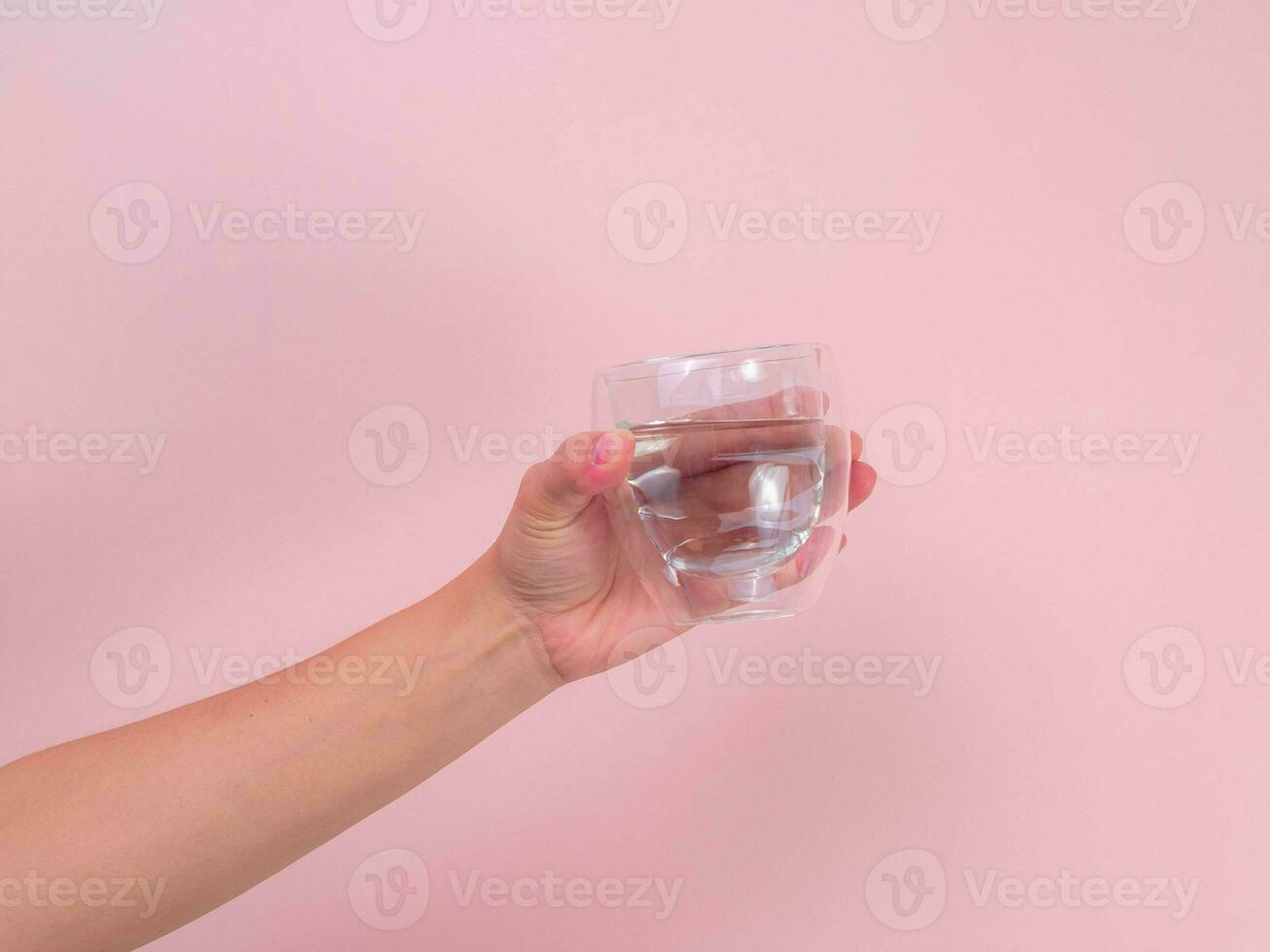 Female hand holding glass of water isolated on pink background. photo