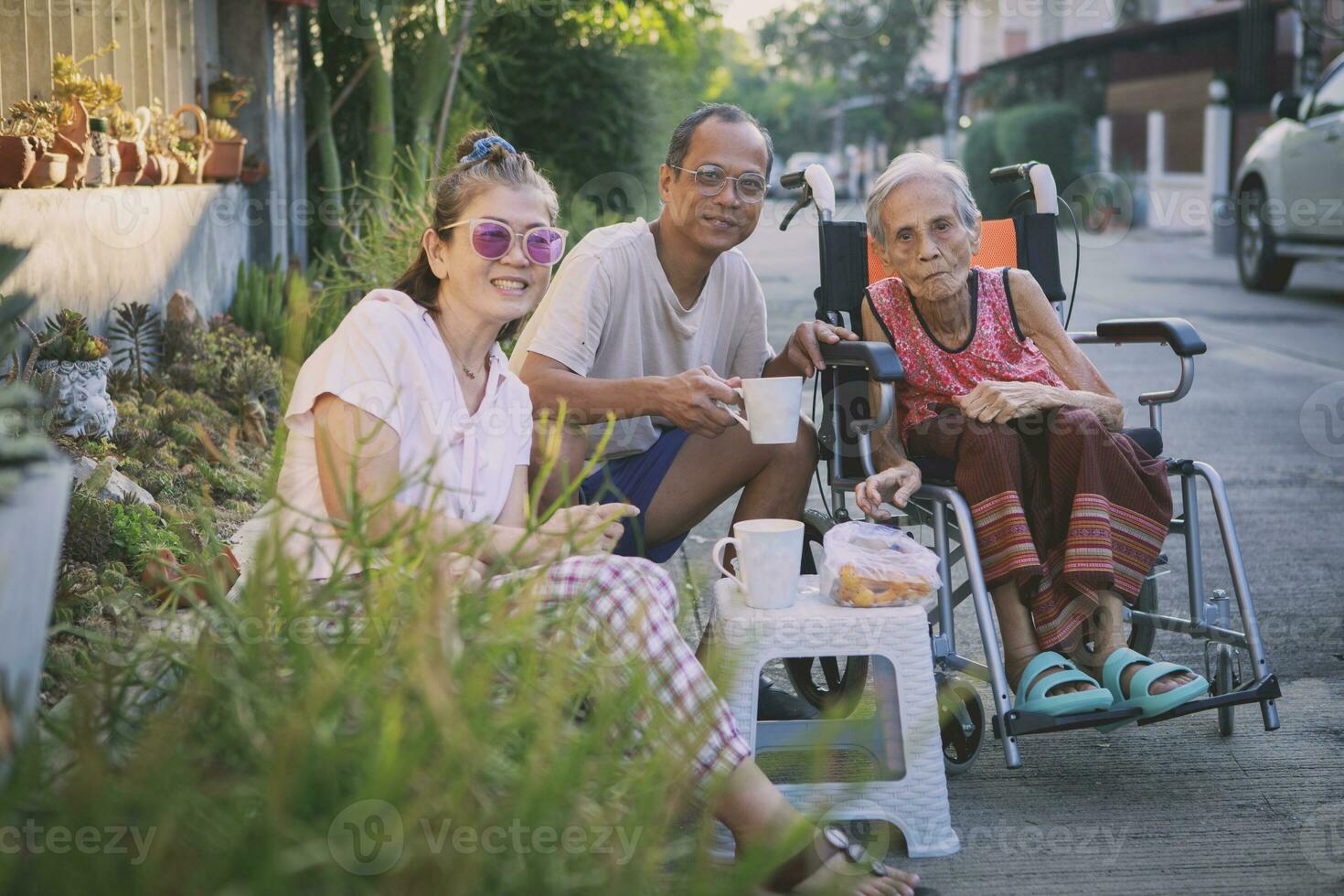 asiático familia con grandioso mamá sentado en rueda silla disfrutar Mañana café a hogar pueblo foto