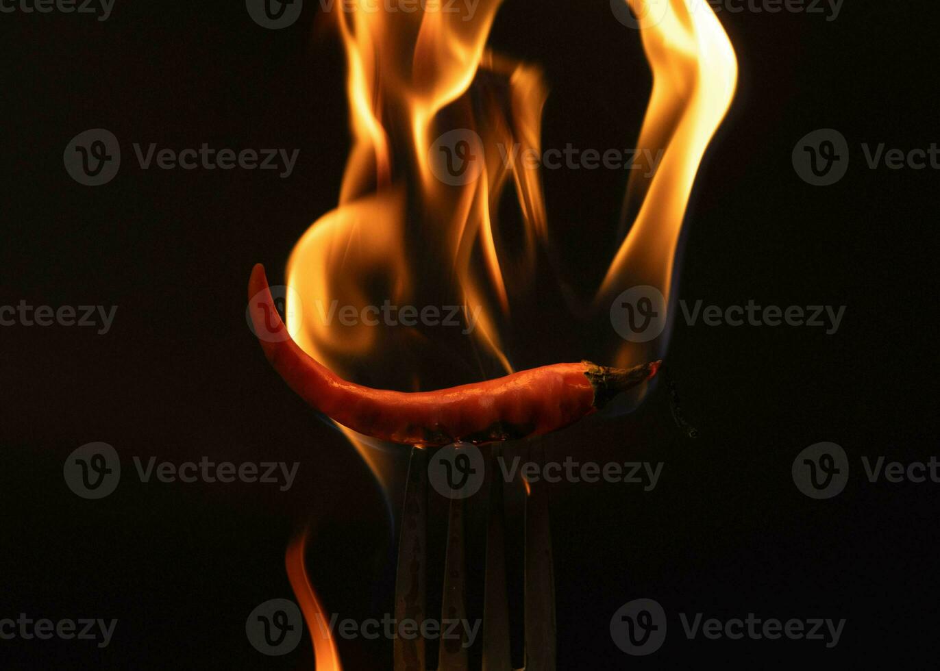 Chili pepper on fork with flames on black background. Burning red chili pepper. Slow motion photo