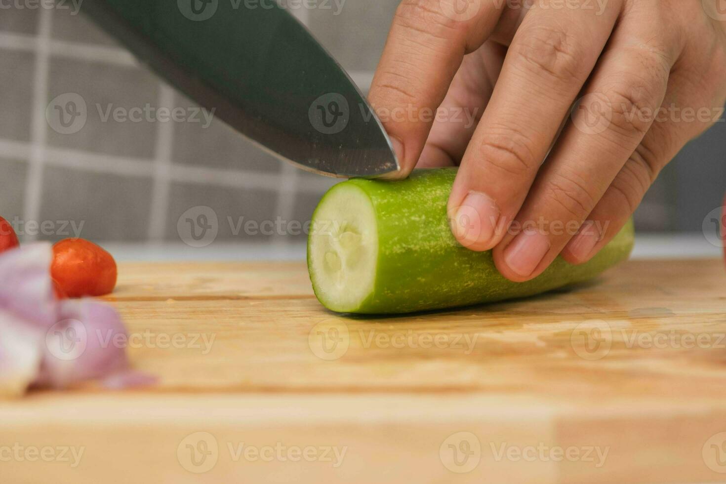 Female hand using a knife to slice cucumbers on a cutting board. Close-up. Woman with kitchen knife cutting cucumber at home. Preparing homemade food photo