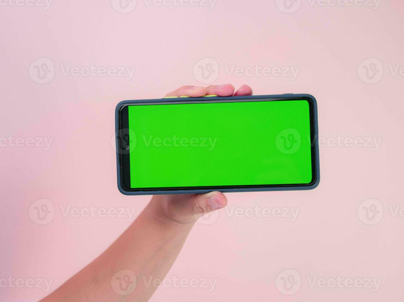 Human hand holding mobile smartphone with green screen in horizontal position isolated on pink background. clipping path photo