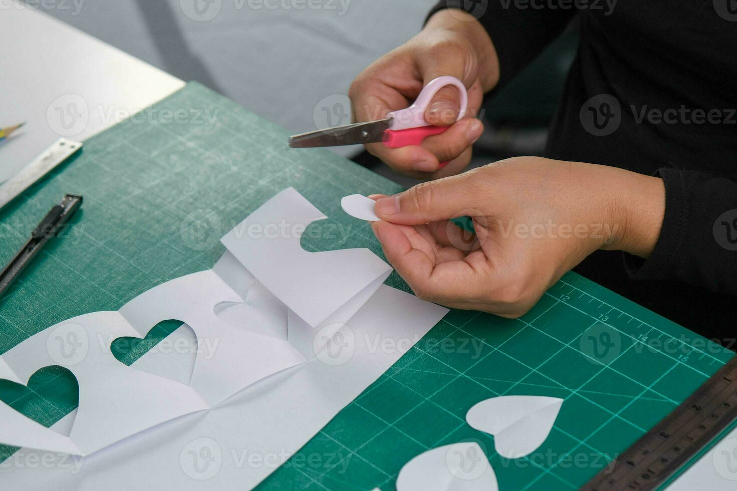 A woman cuts out a white heart-shaped paper with scissors to decorate. Valentine's day greeting card or holiday gift concept. photo