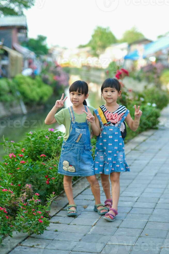 Two cute little sisters smiling and looking at the camera along the Khlong Mae Kha. A waterfront village that has recently been transformed into a new night market in Chiang Mai, Thailand. photo