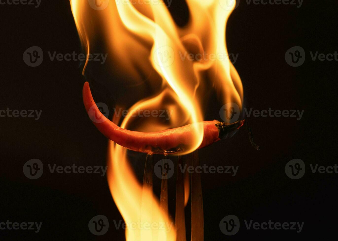 Chili pepper on fork with flames on black background. Burning red chili pepper. Slow motion photo