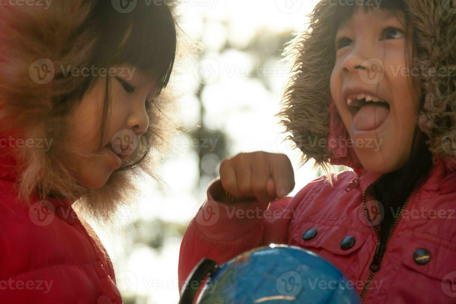 Two cute Asian girls learning a model of the world on nature background and warm sunlight in the park. Children learn through educational play activities. Earth day. World environment day. photo