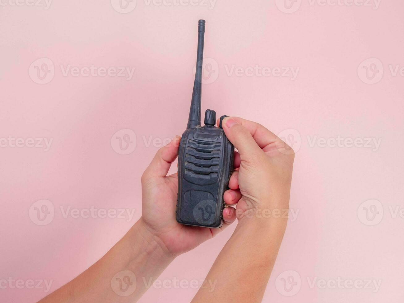 Close up hand holding portable walkie talkie isolated on pink background. Black handheld walkie talkie photo