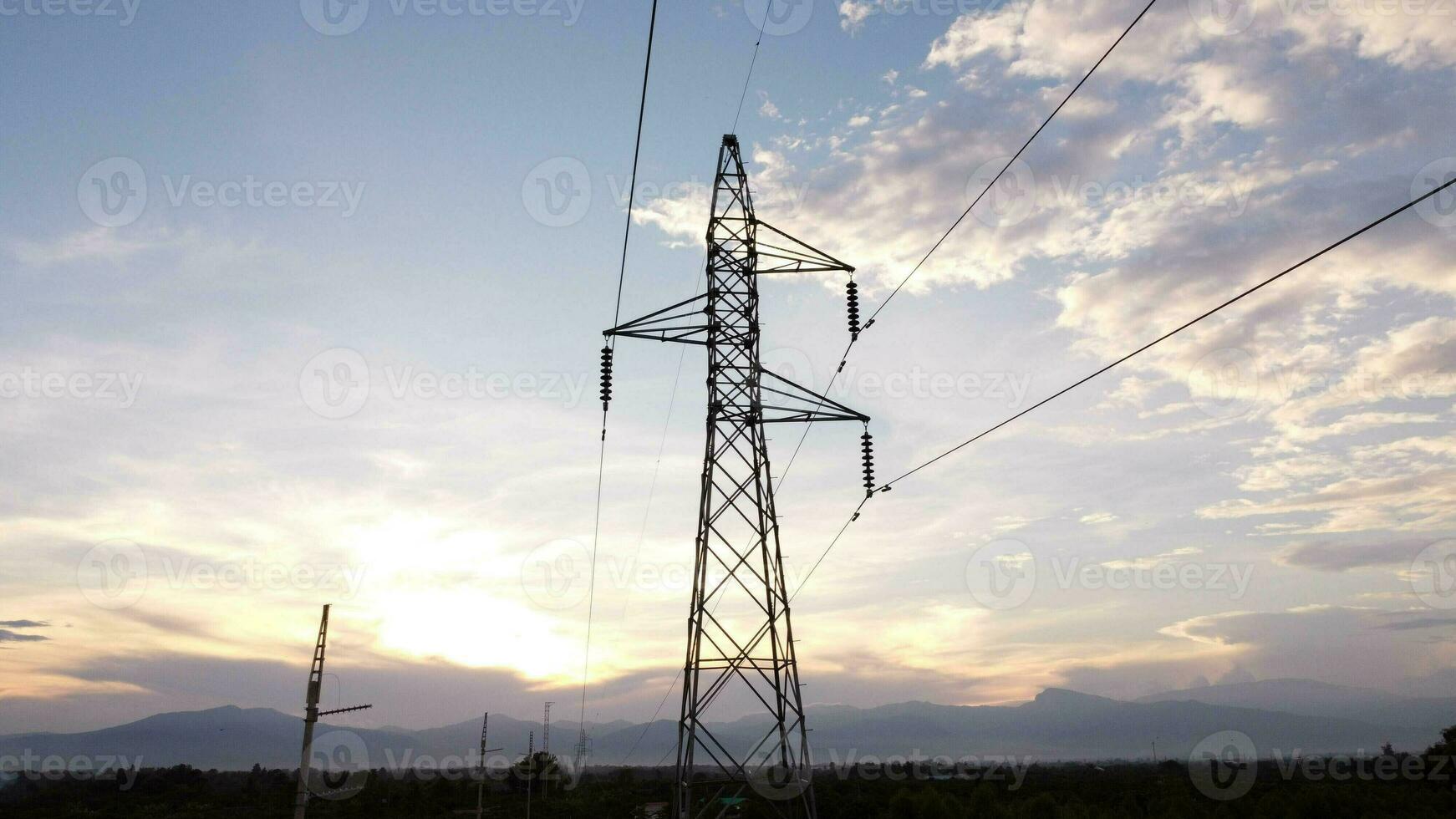 Aerial view of high voltage pylons and wires in the sky at sunset in the countryside. Drone footage of electric poles and wires at dusk. photo