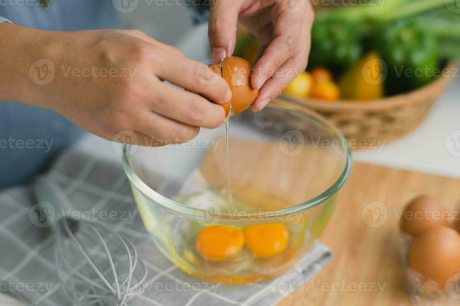 Young woman cooking in a bright kitchen, hand made cracked fresh egg yolks dripping into the bowl. Preparing ingredients for healthy cooking. Homemade food photo