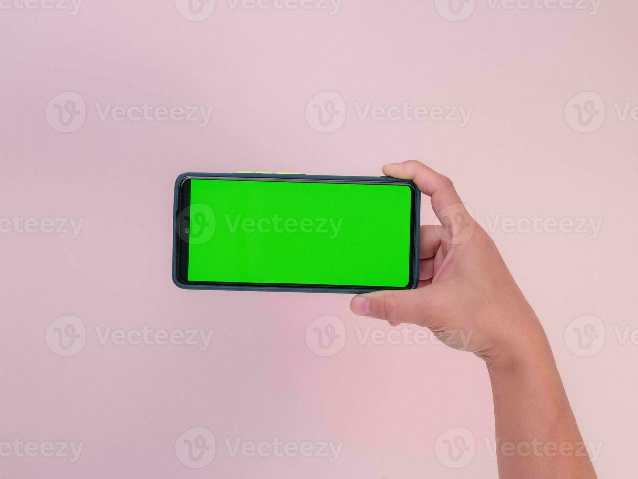 Human hand holding mobile smartphone with green screen in horizontal position isolated on pink background. clipping path photo