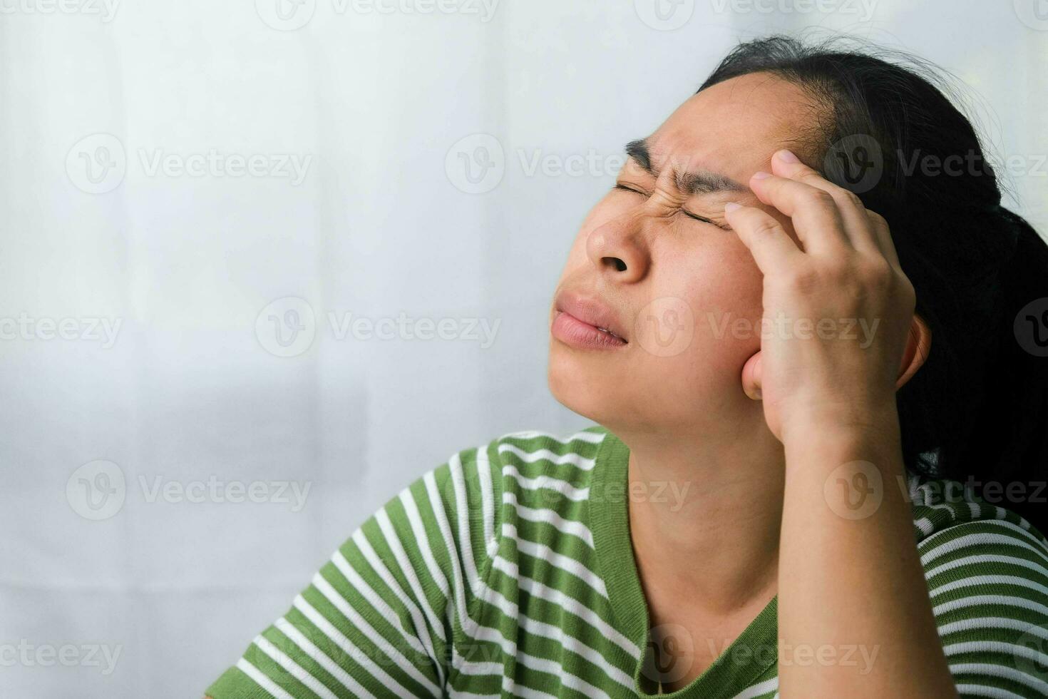 Young woman having headache against white curtain background in room. An adult woman touching head because of headache or migraine. Hands on head. photo
