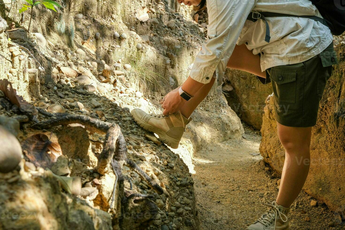Female geologist tying shoelaces while examining nature, analyzing rocks or pebbles. Researchers collect samples of biological materials. Environmental and ecology research. photo