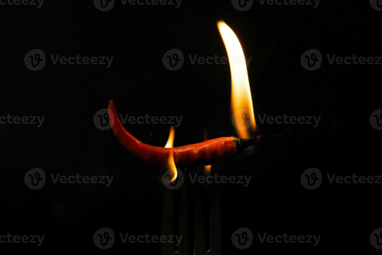 Chili pepper on fork with flames on black background. Burning red chili pepper. Slow motion photo