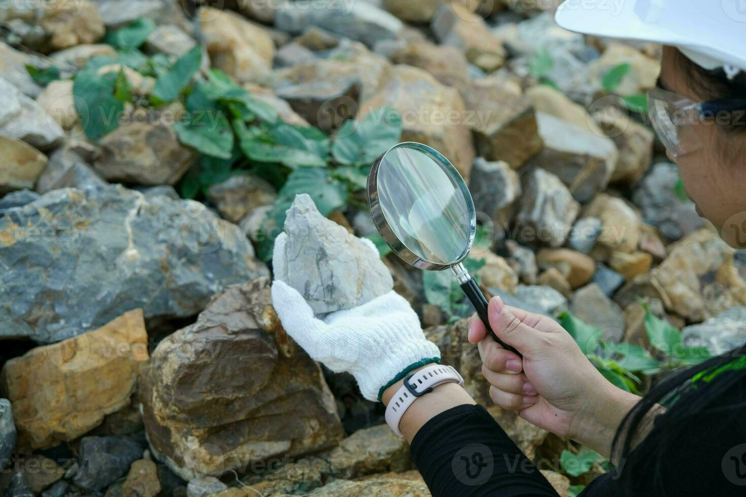 Female geologist using a magnifying glass examines nature, analyzing rocks or pebbles. Researchers collect samples of biological materials. Environmental and ecology research. photo
