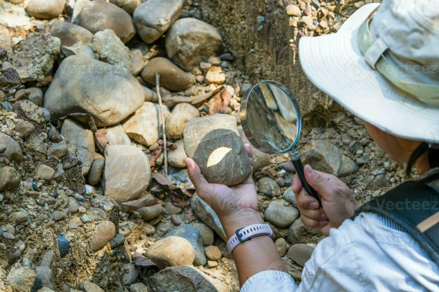 Female geologist using a magnifying glass examines nature, analyzing rocks or pebbles. Researchers collect samples of biological materials. Environmental and ecology research. photo