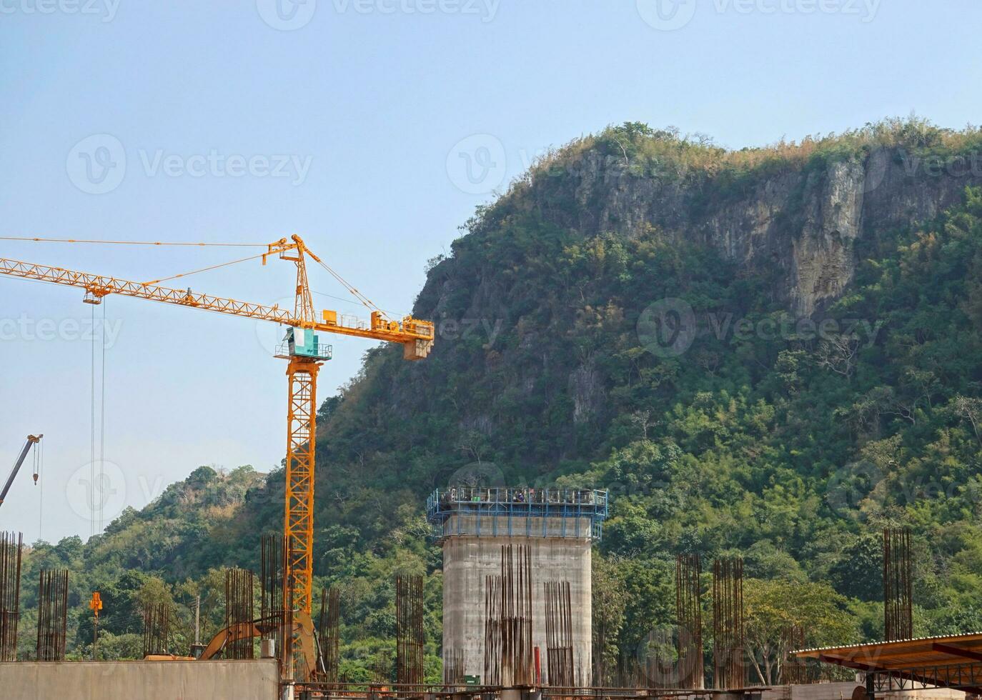 A yellow huge tower crane behind a green forest against a mountain. Construction and development of cities. photo