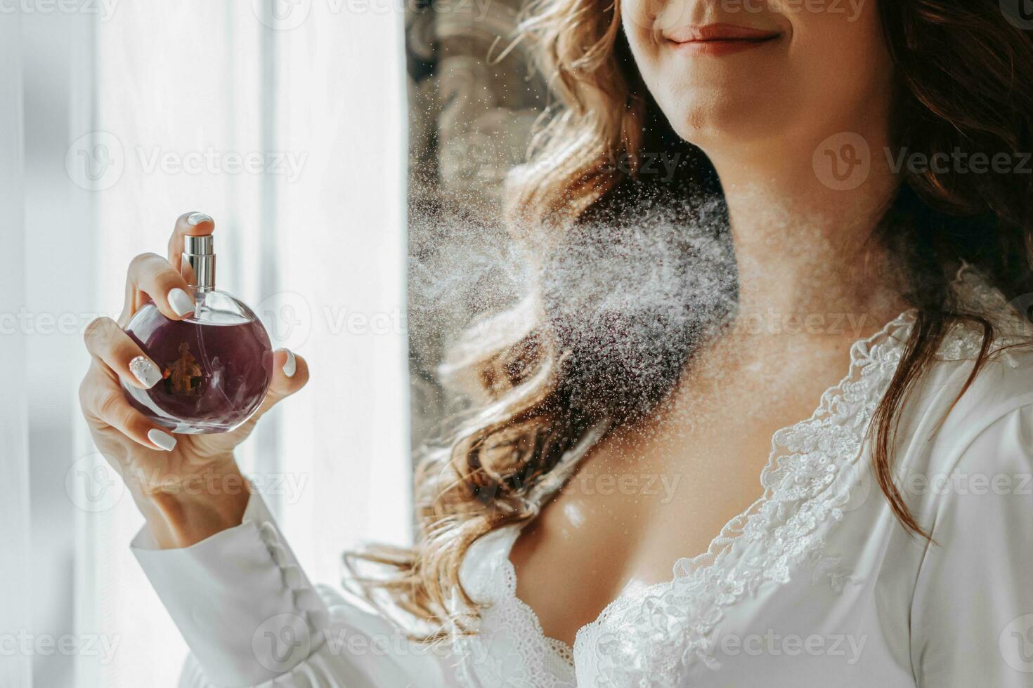 a girl in a white open dress holds purple perfume in her hands and sprays it on herself. Close-up photo