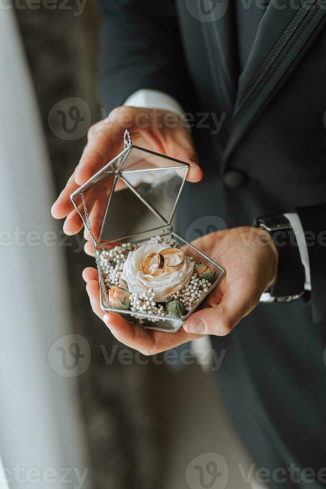 wedding rings in the hands of an adult man decorated in a glass box and various flowers photo