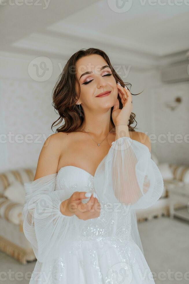 a fragile and elegant bride with long brown hair in a wedding dress poses for a photographer. A child in a hotel room. Portrait with natural light photo
