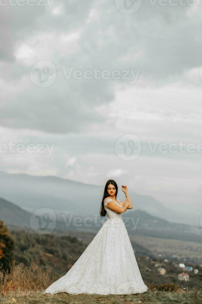 hermosa novia en contra el antecedentes de otoño montañas en frente. un lujoso blanco vestido. Boda ceremonia en parte superior de el montaña. gratis espacio. foto