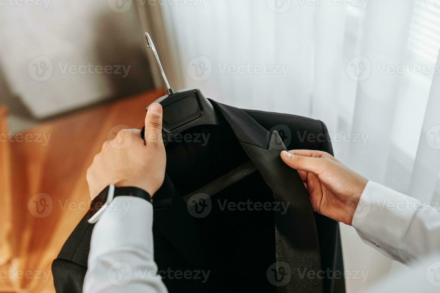 un del hombre manos sostener un negro chaqueta en un percha por el ventana en su habitación. preparación para el Boda ceremonia. de cerca foto de manos