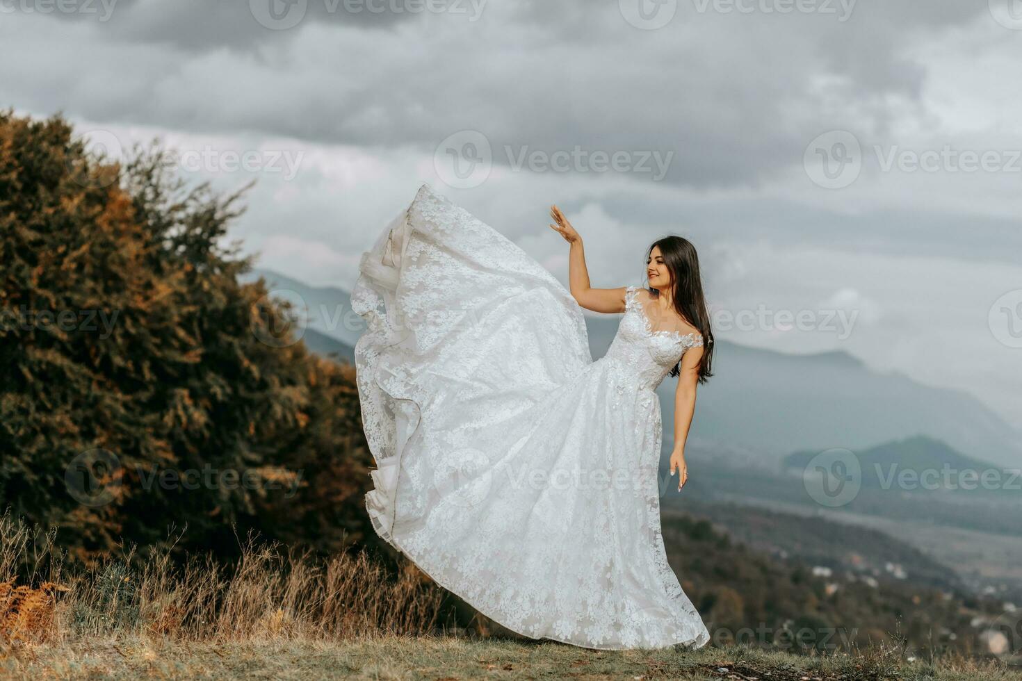 Beautiful bride against the background of autumn mountains in front. A luxurious white dress flutters. Wedding ceremony on top of the mountain. Free space. photo