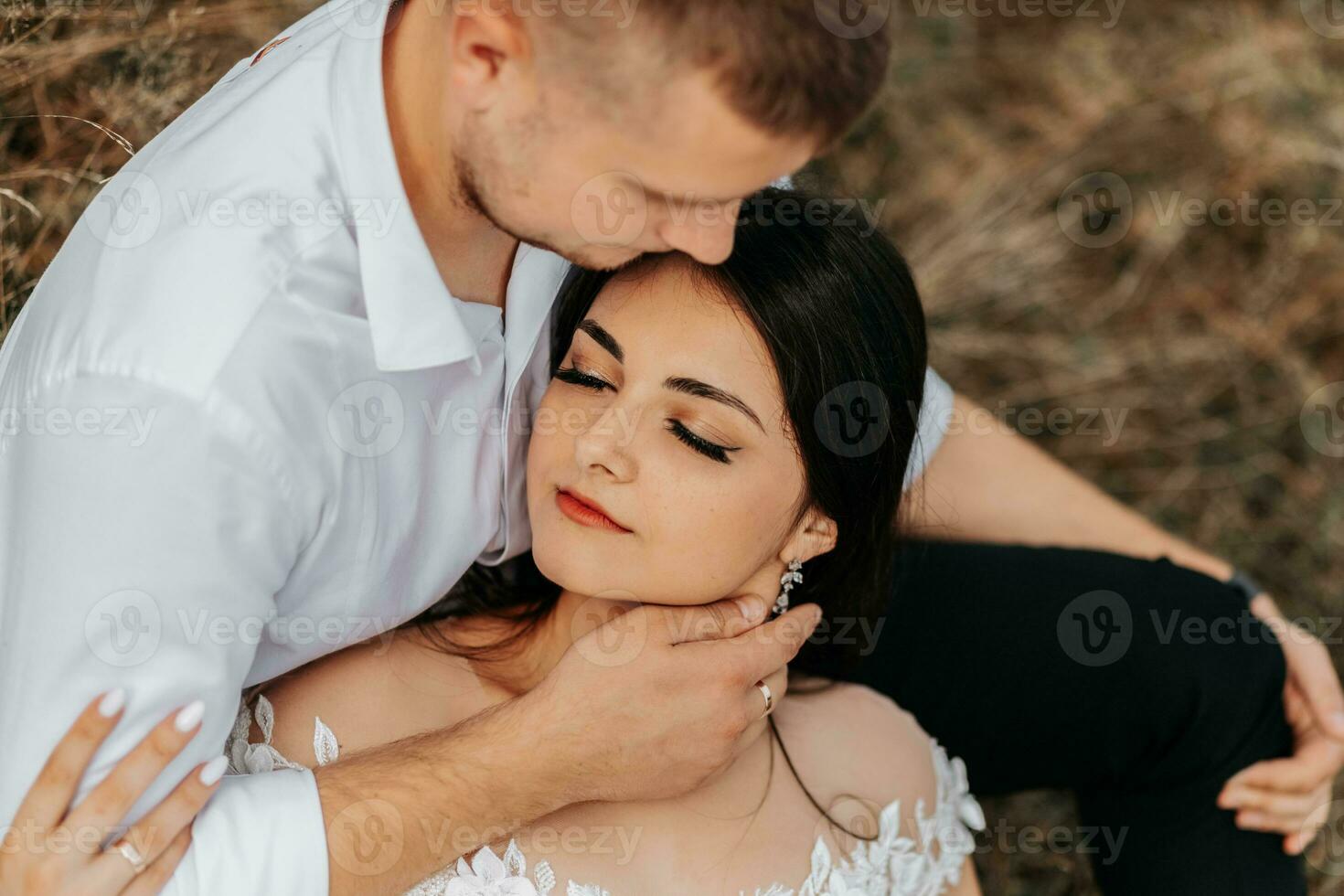 novio y novia mentira en seco césped y abrazo, mujer en un blanco Boda vestido. hermosa otoño Boda foto. el novio objetivos a su frente foto