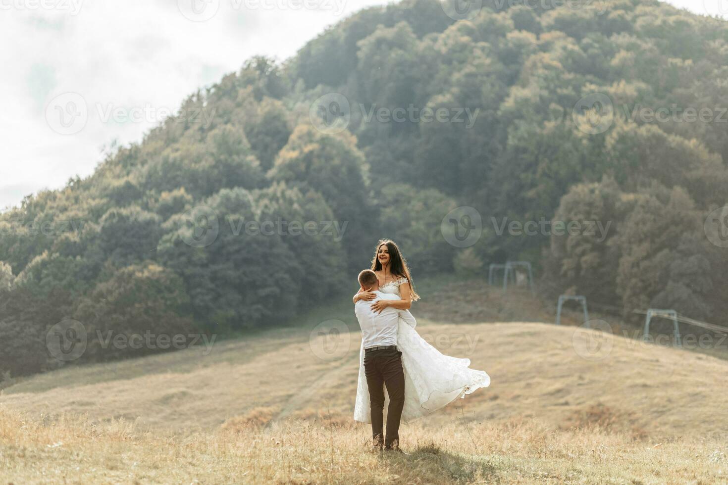 Wedding couple, walks in the mountains. Photo of a wide plan. Free space. The groom spins the bride in his arms, the bride's dress develops in the wind.