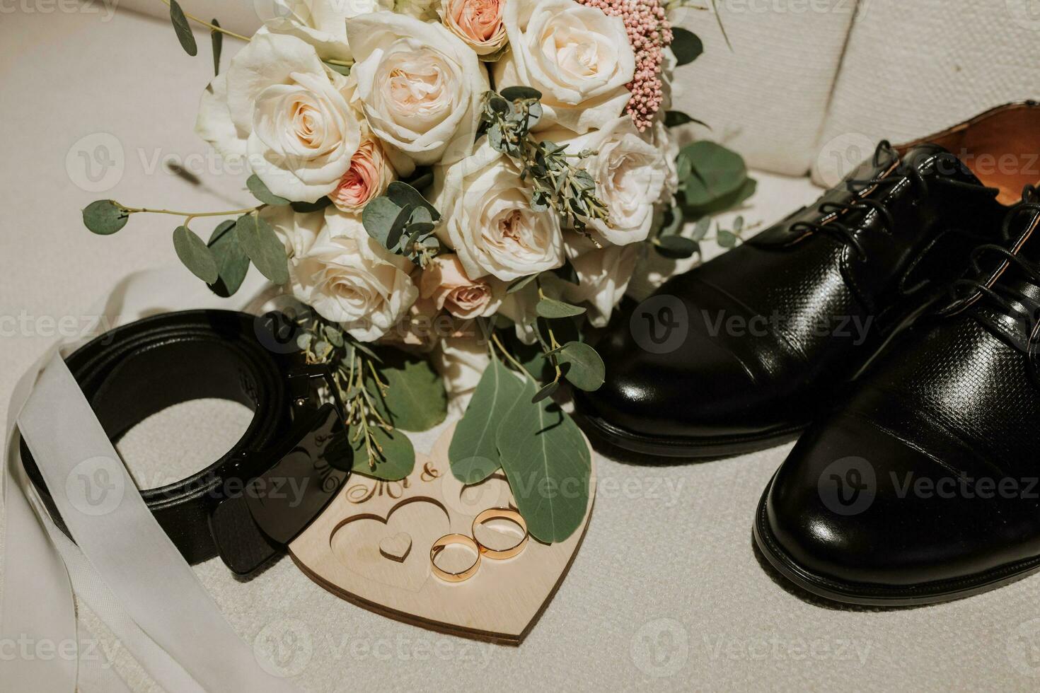 details of the groom are arranged in a composition. Black shoes, wedding bouquet, gold wedding rings on a wooden stand, black men's belt photo