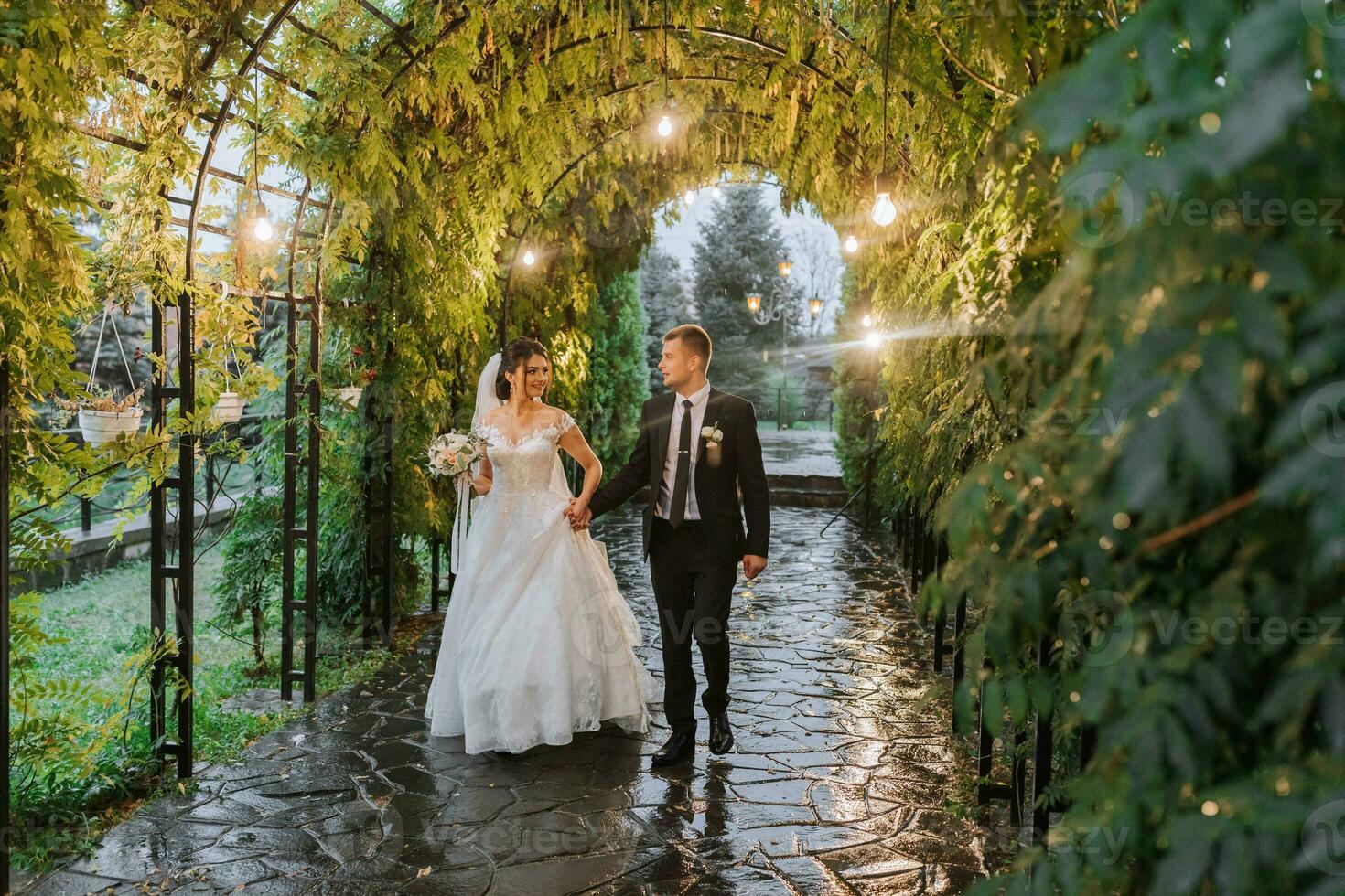 el novia y novio son caminando en el noche parque con un ramo de flores de flores y verdor, verdor en naturaleza. romántico Pareja de recién casados al aire libre. Boda ceremonia en el botánico jardín. foto