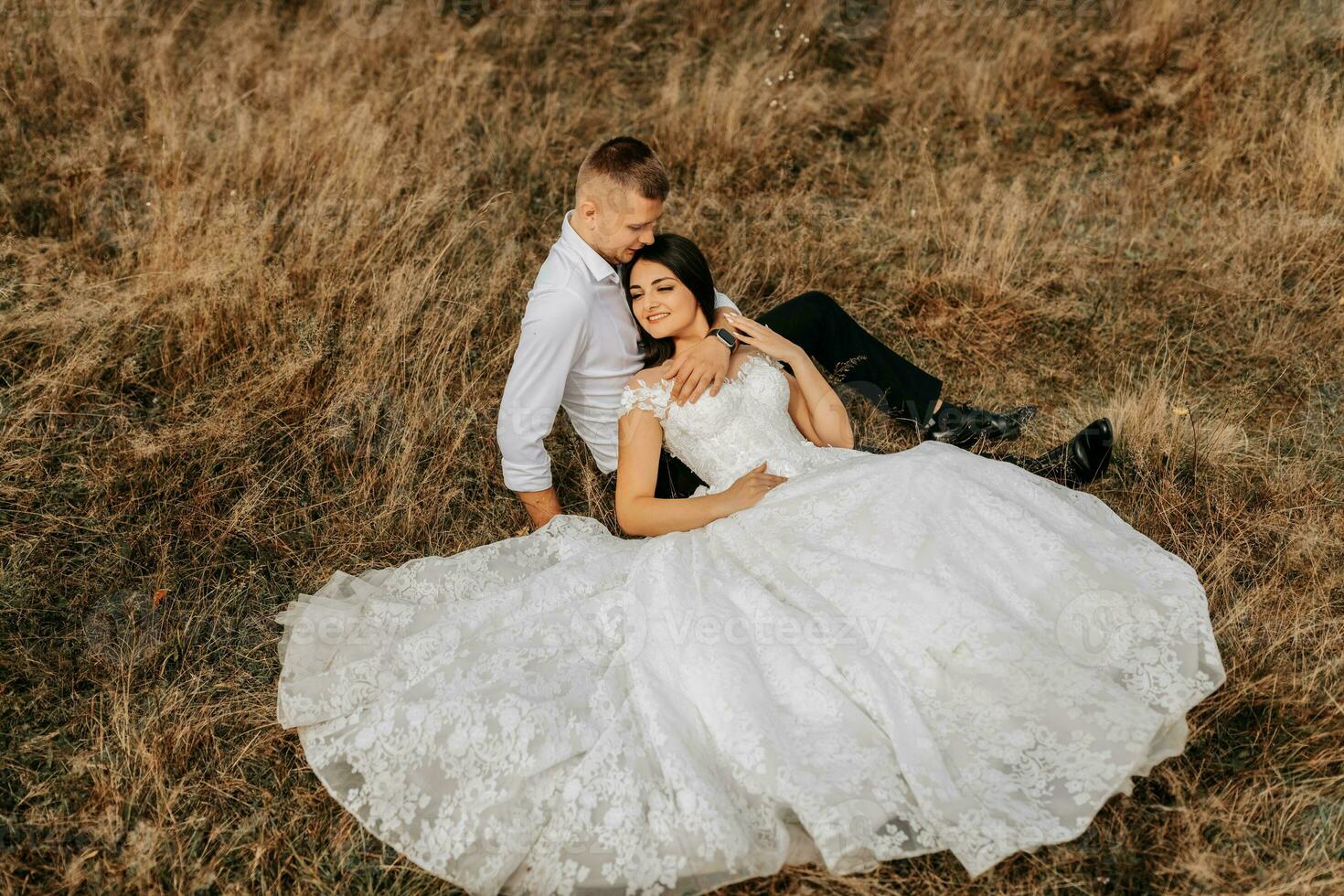 el novia y novio son acostado en el seco césped y abrazando, un mujer en un blanco Boda vestido. hermosa otoño Boda foto. foto