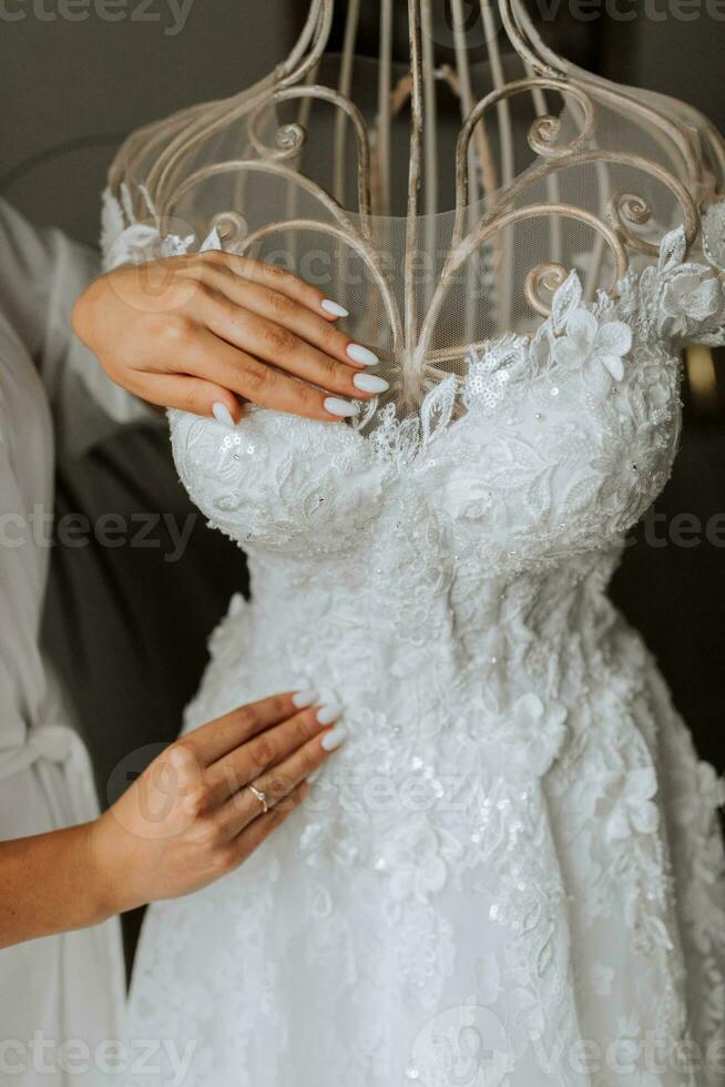 Portrait of the bride with studio light in her room. A girl in a white robe demonstrates her wedding dress on a mannequin. Hands close up photo