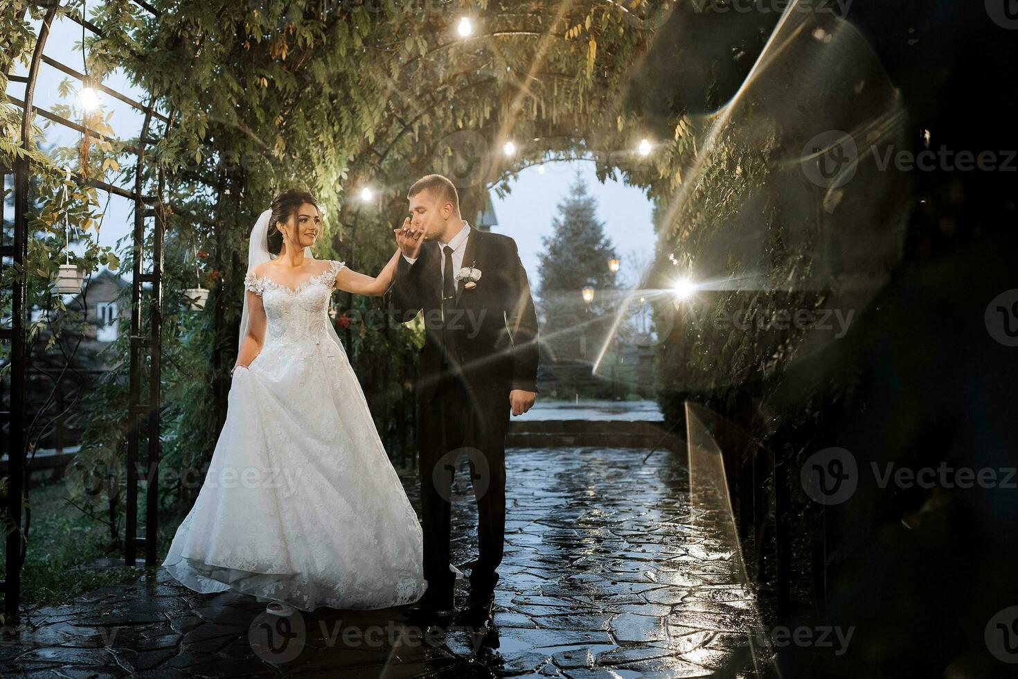 The bride and groom are walking in the evening park with a bouquet of flowers and greenery, greenery in nature. Romantic couple of newlyweds outdoors. Wedding ceremony in the botanical garden. photo