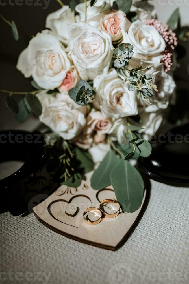 details of the groom are arranged in a composition. Black shoes, wedding bouquet, gold wedding rings on a wooden stand, black men's belt photo