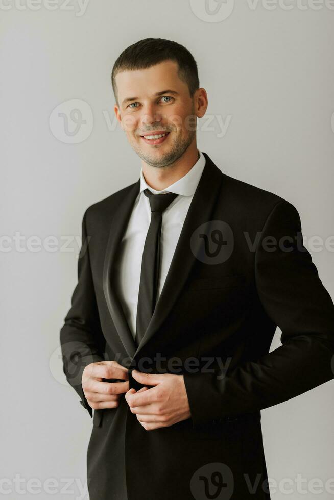 portrait of a young man in a white shirt and tie putting on his black jacket. The groom is preparing for the wedding ceremony. photo