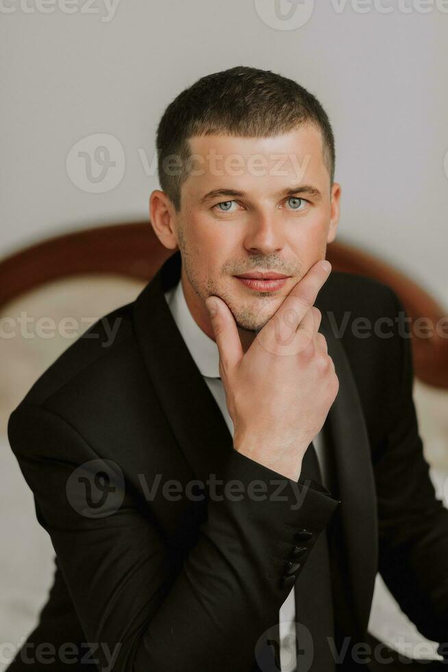 portrait of a young man in a white shirt and tie holding his chin with his hand. The groom is preparing for the wedding ceremony. photo