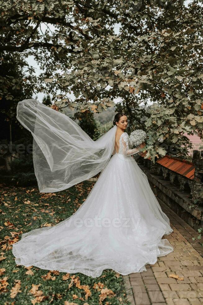 Full-length portrait of the bride with a long train and a bouquet of flowers in her hands, veil blowing in the wind photo