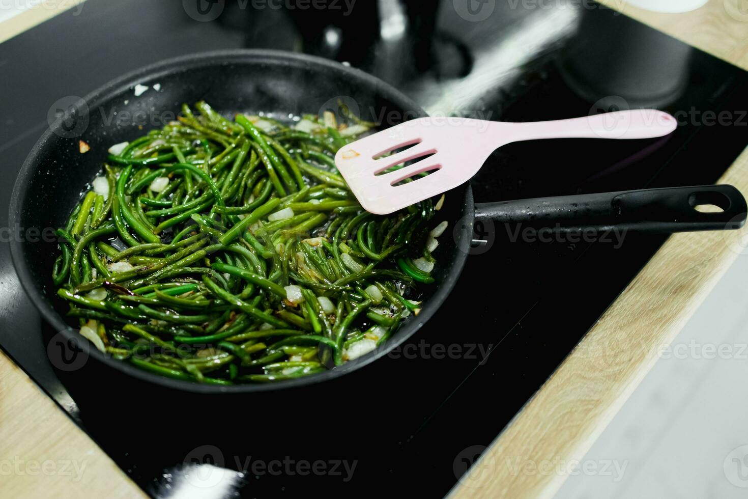 cooking greens, asparagus, garlic bunches, on a black pan and an electric stove, close-up photo