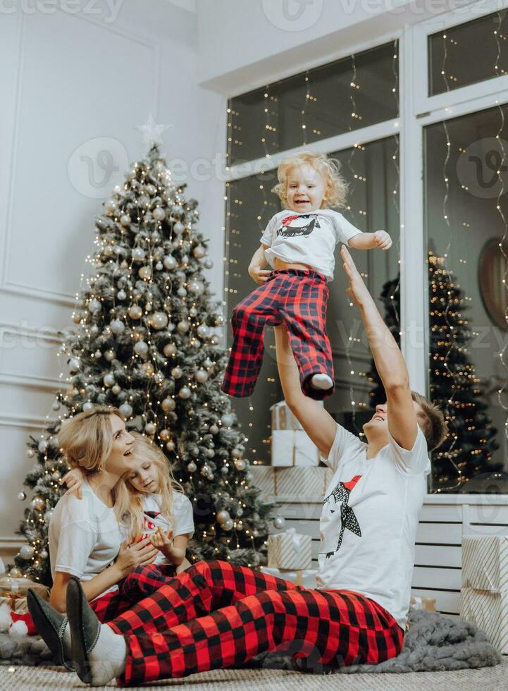 Cheerful and happy family with Christmas gifts near the Christmas tree in matching pajamas. Children are having fun. Loving family with gifts in the room. photo