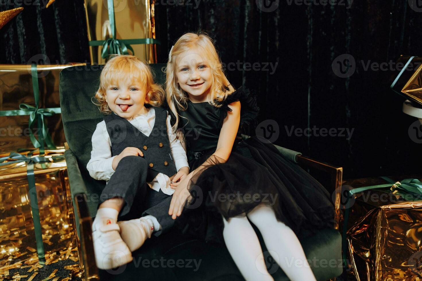 Merry Christmas and Happy Holidays. Cheerful cute children, a girl and a boy. Children are having fun on a chair near gifts. Loving family with gifts in the room. photo