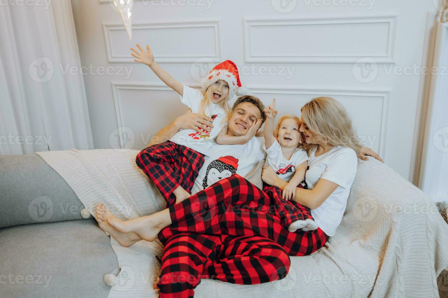 Cheerful and happy family in identical pajamas lying on the sofa. Children are having fun. Loving family with gifts in the room. photo
